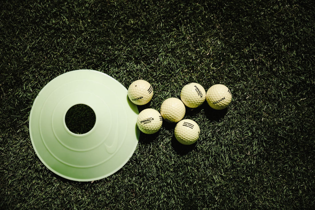 White golf balls and a training cone placed on vibrant green grass, ready for practice.