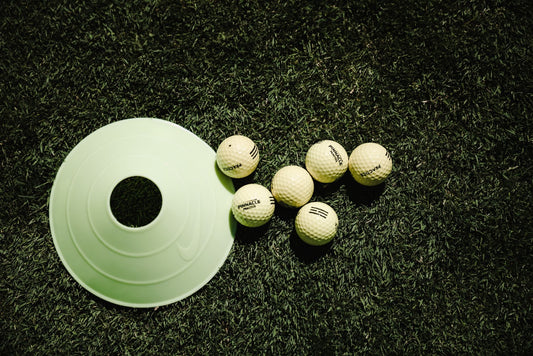 White golf balls and a training cone placed on vibrant green grass, ready for practice.