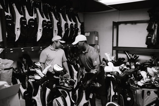 Two men sorting and organizing golf bags and clubs in a storage room.
