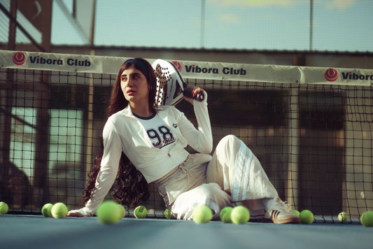 Young woman tennis player sitting on court, surrounded by tennis balls, in vibora club setting.