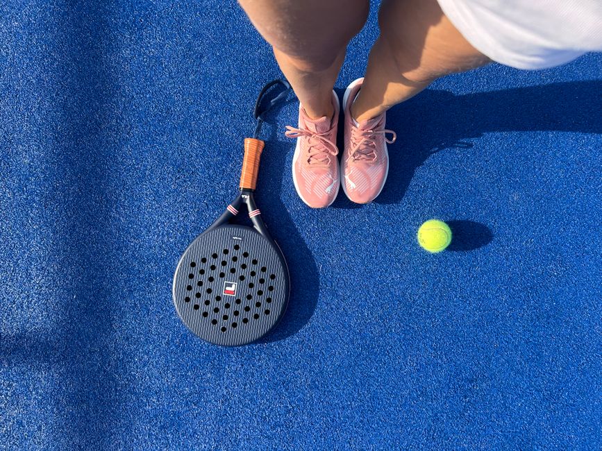 Top view of a padel player with shoes, racket, and ball on a vibrant blue court.