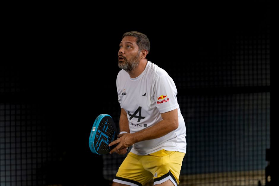 Focused man playing padel on an indoor court wearing a sporty outfit.