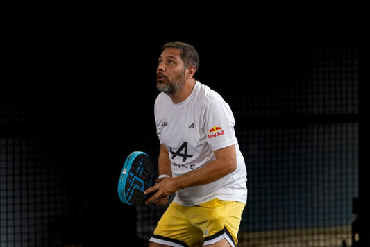 Focused man playing padel on an indoor court wearing a sporty outfit.