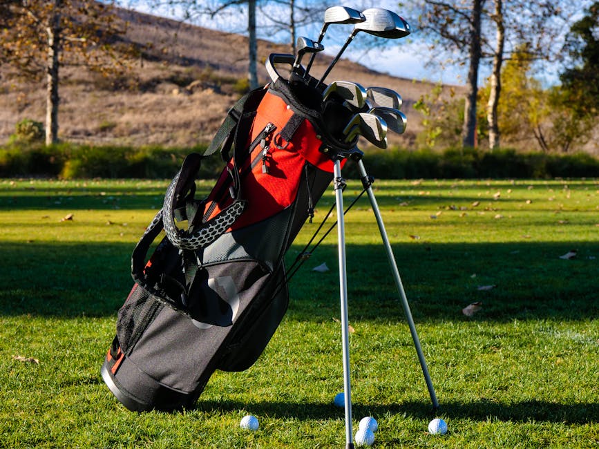 Red and black golf bag with clubs on a sunny golf course lawn outdoors.