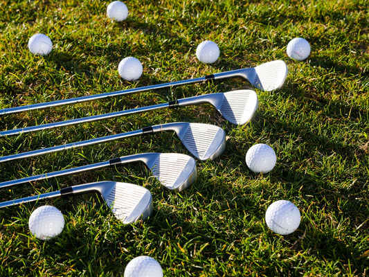 Close-up of golf clubs and balls scattered on green grass, perfect for sports equipment use.